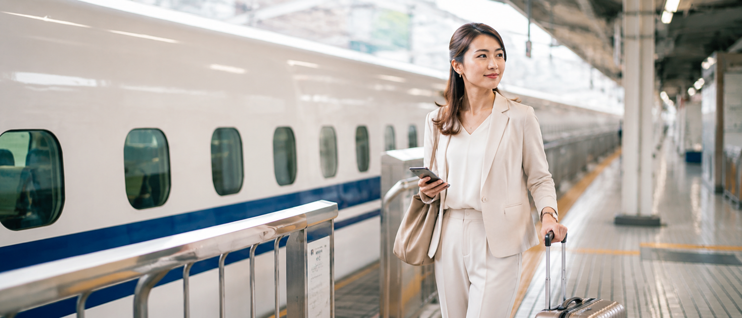 新幹線のホームでキャリーケースを引きながら移動する女性。国内出張やビジネストラベルをイメージしたシーン