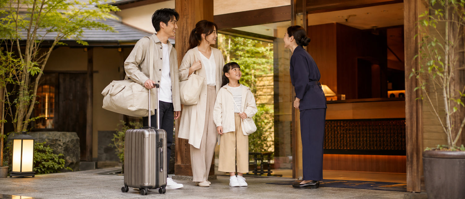 旅行バッグとキャリーケースを持って宿泊施設を訪れる家族。1泊2日などの短期旅行をイメージしたシーン